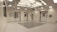 An empty, well-lit, modern operating room with white walls and ceiling. Various surgical lights and equipment are suspended from the ceiling. The room has a clean and sterile appearance with closed doors and built-in shelves.