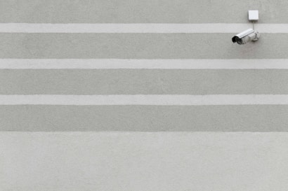 A series of horizontal stripes in light gray and green colors on a textured wall with a surveillance camera mounted on the upper right corner.