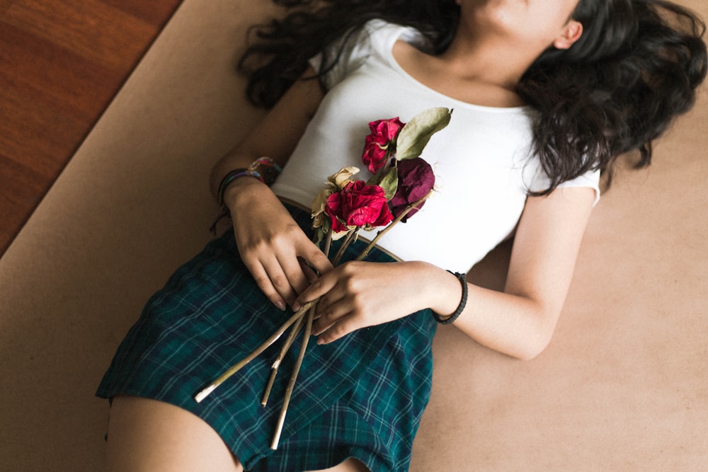woman lying on brown rug holding red roses