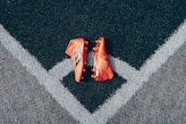A pair of bright orange soccer cleats is placed on a textured black and gray surface, positioned symmetrically along intersecting white lines that form a V shape.