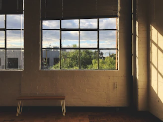 A sunlit divided window bench with cushions and a hexagonal mirror hanging above.