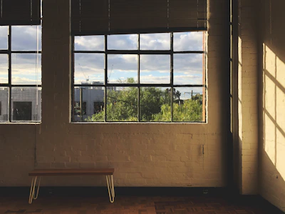 A sunlit divided window bench with cushions and a hexagonal mirror hanging above.