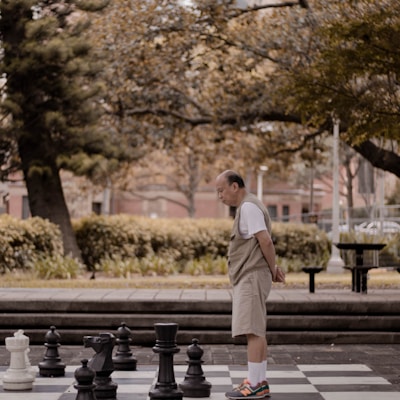 man standing on big chessboard with chest pieces at park