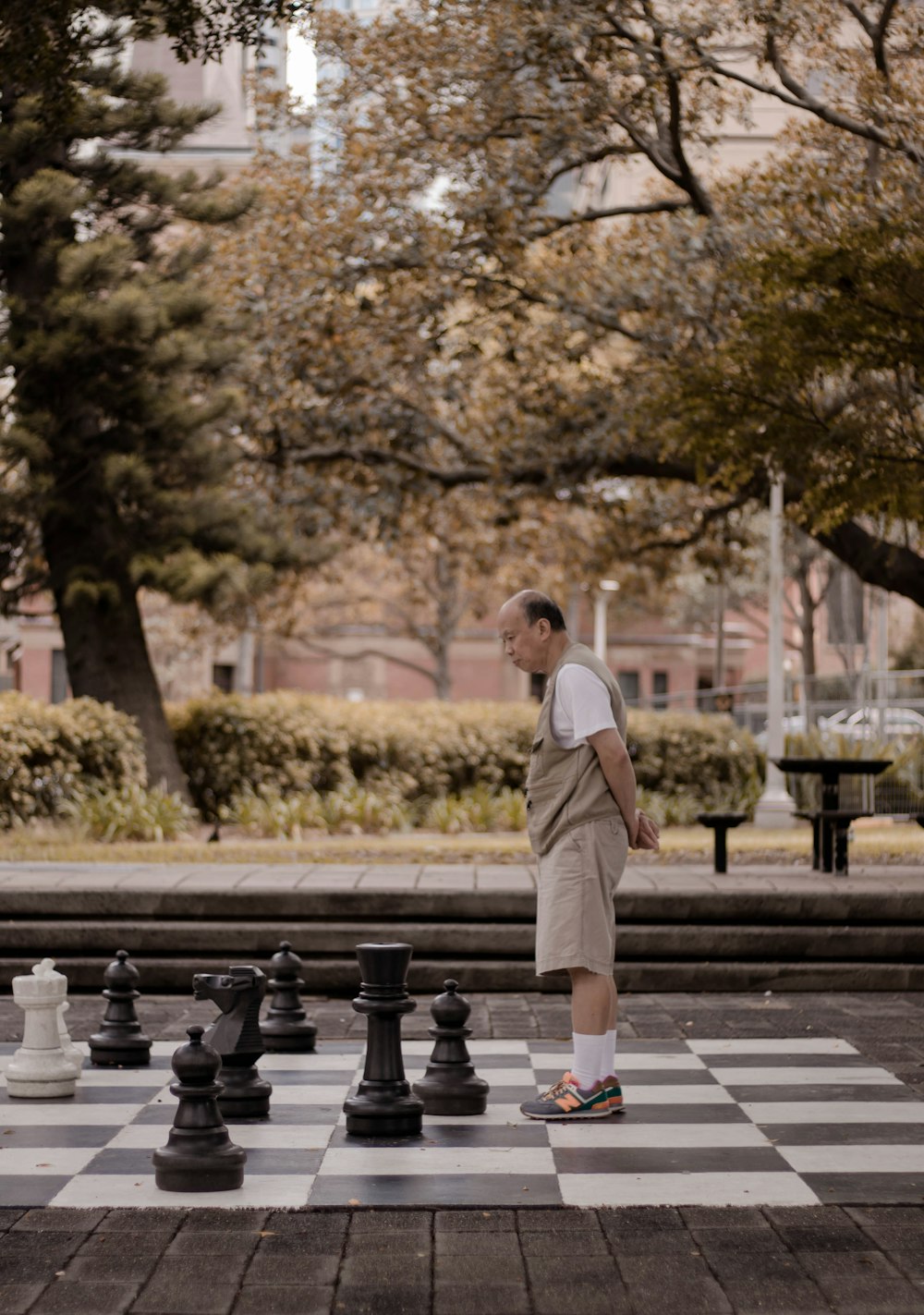 Homem em pé no grande tabuleiro de xadrez com peças no peito no parque