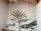 A mural painted on a wall depicts a tree with green leaves and yellow flowers. Large stones form an abstract pattern along the wall, and a small sculpture or painting of a brown squirrel is perched on one of the stone formations. The ceiling features exposed wooden beams and decorative branches.