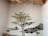 A mural painted on a wall depicts a tree with green leaves and yellow flowers. Large stones form an abstract pattern along the wall, and a small sculpture or painting of a brown squirrel is perched on one of the stone formations. The ceiling features exposed wooden beams and decorative branches.