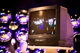 A vintage Sony Trinitron television is placed on a stand, displaying a blurred scene of lights and figures, possibly from a cityscape. The background features multiple reflective spheres, creating an artistic and modern ambiance.