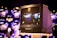 A vintage Sony Trinitron television is placed on a stand, displaying a blurred scene of lights and figures, possibly from a cityscape. The background features multiple reflective spheres, creating an artistic and modern ambiance.