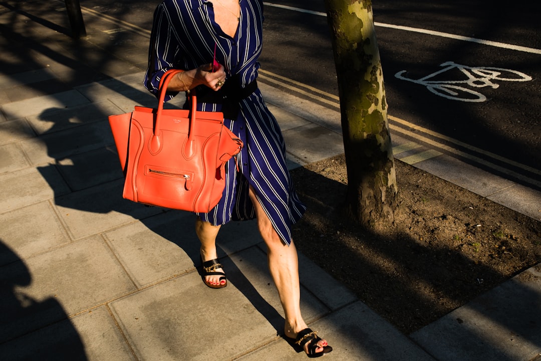 woman wearing blue dress with orange leather bag walking at the sidewalk