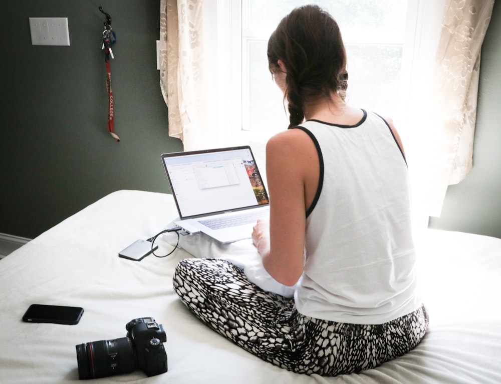 mulher na regata branca sentada na cama na frente do computador portátil