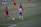 A women's soccer match is underway on a grass field. Players in red and black striped uniforms and others in white and blue uniforms are actively engaged in the game, with two players focused on controlling the ball near them.