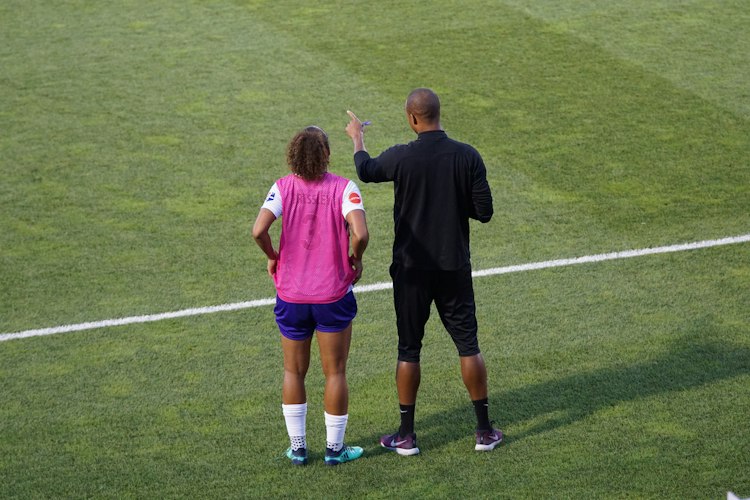 Coach standing on the sideline reviewing a tablet showing player statistics during a game