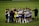 A group of soccer players and staff huddle together on a field, forming a tight circle. They are dressed in uniforms with some individuals in white and purple jerseys, while others wear black or yellow. The atmosphere seems focused and possibly motivational.