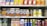 A supermarket shelf displays a variety of packaged drinks, including milk tea, lemon tea, apple juice, orange juice, coffee drinks, and other flavored beverages. The packaging features vibrant colors and images of ingredients such as fruits and coffee beans. Each product is neatly arranged in rows with price tags visible.