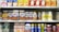 A supermarket shelf displays a variety of packaged drinks, including milk tea, lemon tea, apple juice, orange juice, coffee drinks, and other flavored beverages. The packaging features vibrant colors and images of ingredients such as fruits and coffee beans. Each product is neatly arranged in rows with price tags visible.