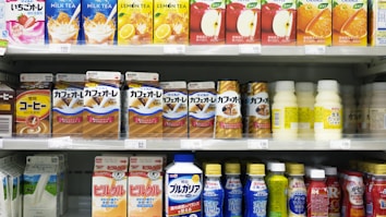 A supermarket shelf displays a variety of packaged drinks, including milk tea, lemon tea, apple juice, orange juice, coffee drinks, and other flavored beverages. The packaging features vibrant colors and images of ingredients such as fruits and coffee beans. Each product is neatly arranged in rows with price tags visible.