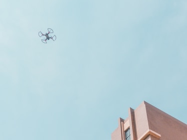 white quadcopter drone fly near brown concrete building