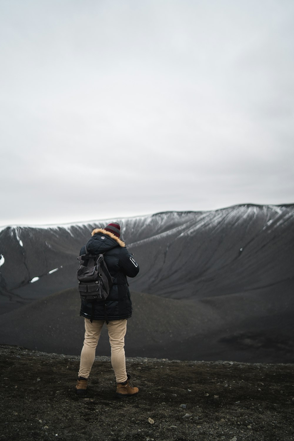 person in black parka jacket standing on brown soil