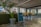 A modern office space with a large green plant in a metallic pot, a motivational sign saying 'Think of Your Own Ideas', and a foosball table. The area has large windows and a glass conference room visible in the background. The interior includes a mix of natural and industrial elements, with visible ceiling beams and a polished concrete floor.