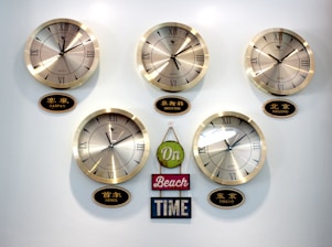 Five wall clocks each displaying different time zones are mounted on a wall, labeled Saipan, Moscow, Beijing, Seoul, and Tokyo. Beneath the clocks, there is a decorative sign with the words 'On Beach Time' in green, pink, and blue hues.