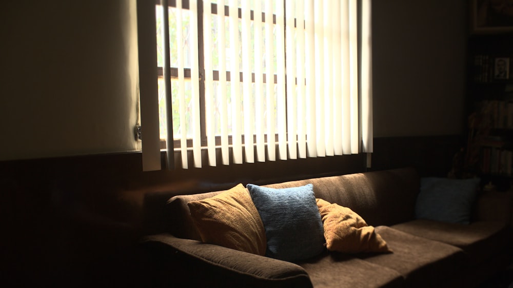 Sofá de 3 plazas de tela marrón frente a las persianas blancas que cubren la ventana