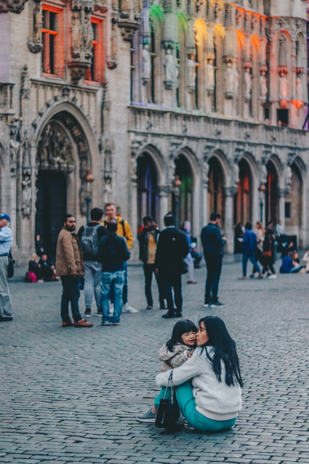 woman kissing girl while sitting near building