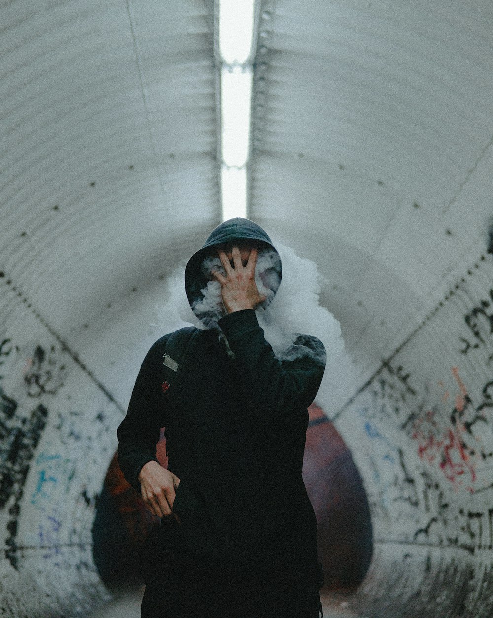 Mann steht in schwarzem Mantel und bedeckt sein Gesicht mit der Hand im Tunnel