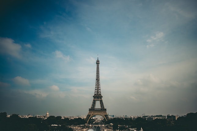 The Eiffel Tower stands tall against a vast, cloudy sky surrounded by the cityscape of Paris, with a soft, muted lighting casting gentle shadows.