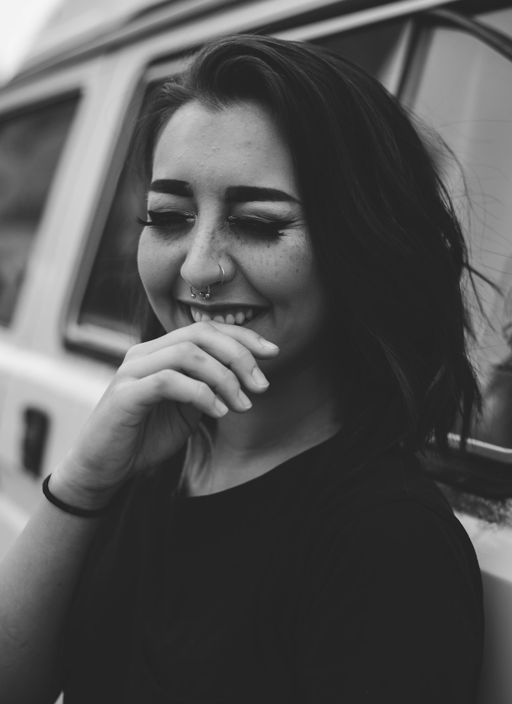 Foto en escala de grises de una mujer sonriendo apoyada en un coche