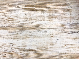 A detailed wood texture featuring horizontal lines and natural grain patterns in a mix of brown and beige hues. The surface exhibits a rustic and weathered appearance.