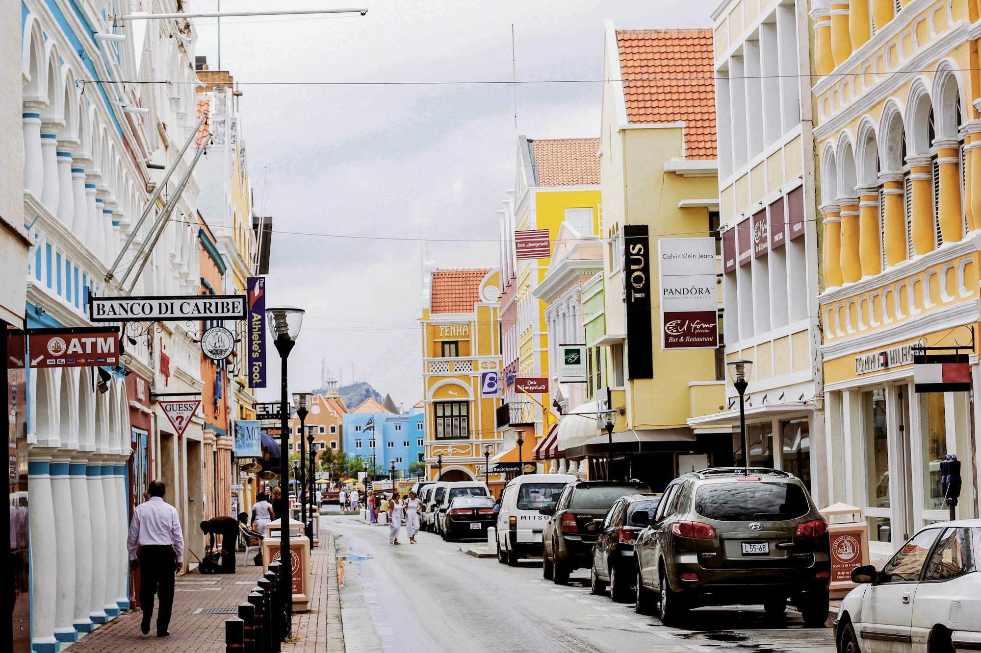 empty street in Willemstad, Curaçao with parked cars and pedestrians walking among colored buildings