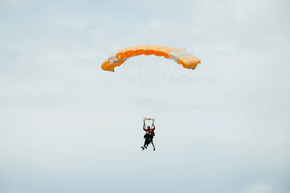 A skydiver in freefall with a vibrant orange parachute opening against a clear blue sky.