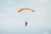 A skydiver in freefall against a bright blue sky, with a vibrant orange parachute opening.