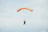 A skydiver in freefall against a bright blue sky, with a vibrant orange parachute opening.