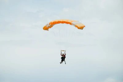 A vibrant shot of a skydiver freefalling with a bright orange parachute against a clear blue sky.