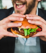 person holding burger bun with vegetables and meat