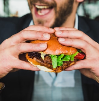 person holding burger bun with vegetables and meat