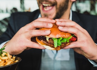 person holding burger bun with vegetables and meat