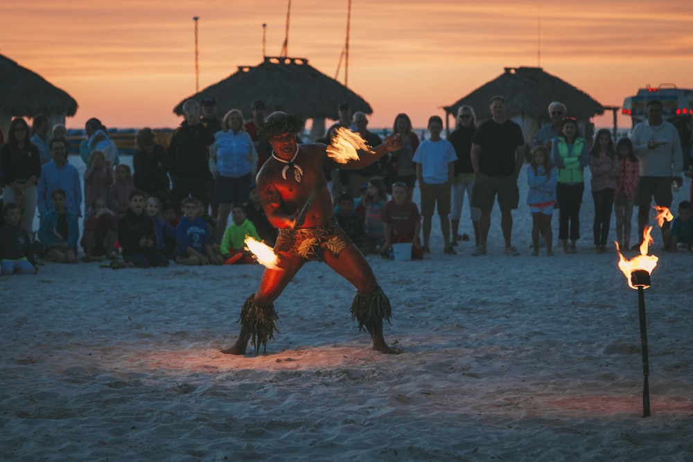 Mann tanzt Feuertanz umgeben von Menschen am Strand