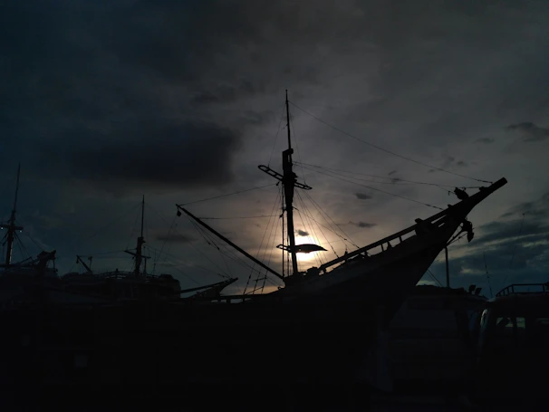 A cinematic frame of a traditional boat sailing against a dramatic cloudy sky at dusk.