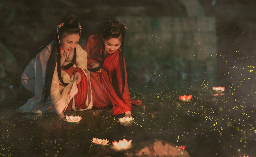흰색과 빨간색의 전통 의상을 입은 두 여성이 꽃을 들고 있습니다.