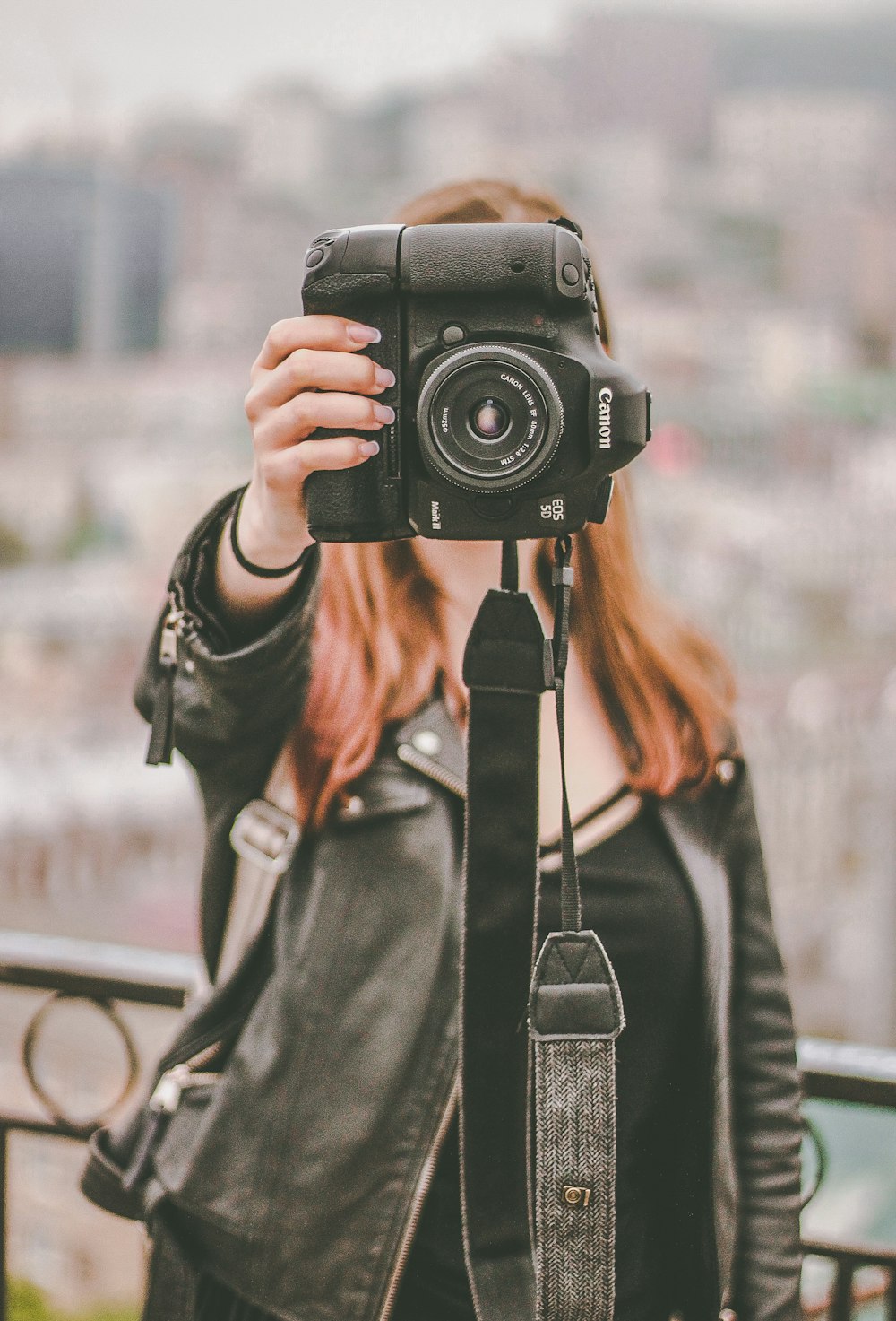 mujer con chaqueta de cuero negro sosteniendo una cámara Canon DSLR negra