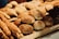 A variety of freshly baked bread and pastries are displayed on a wooden shelf. There are different types of bread rolls, long breadsticks, and some round loaves with a rustic appearance. The baked goods have a golden-brown crust, indicating a well-baked texture.