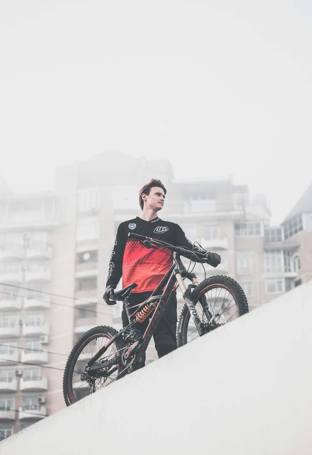 man wearing black and red ombre crew-neck long-sleeved shirt and black gloves standing on platform holding black full-suspension bike