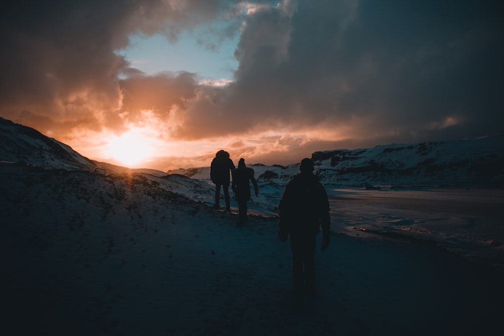 silhouette of three person mountaineering with snow-covered mountains