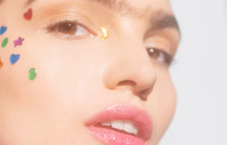 Close-up of a smiling woman applying a small skin patch near her eye in soft natural light.