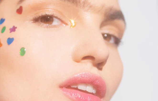 Close-up of a smiling woman applying a small skin patch near her eye in soft natural light.