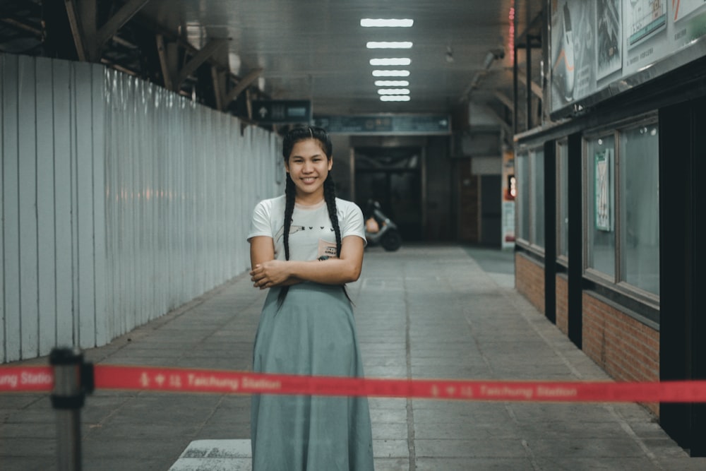 smiling woman wearing grey shirt and skirt standing near concrete building