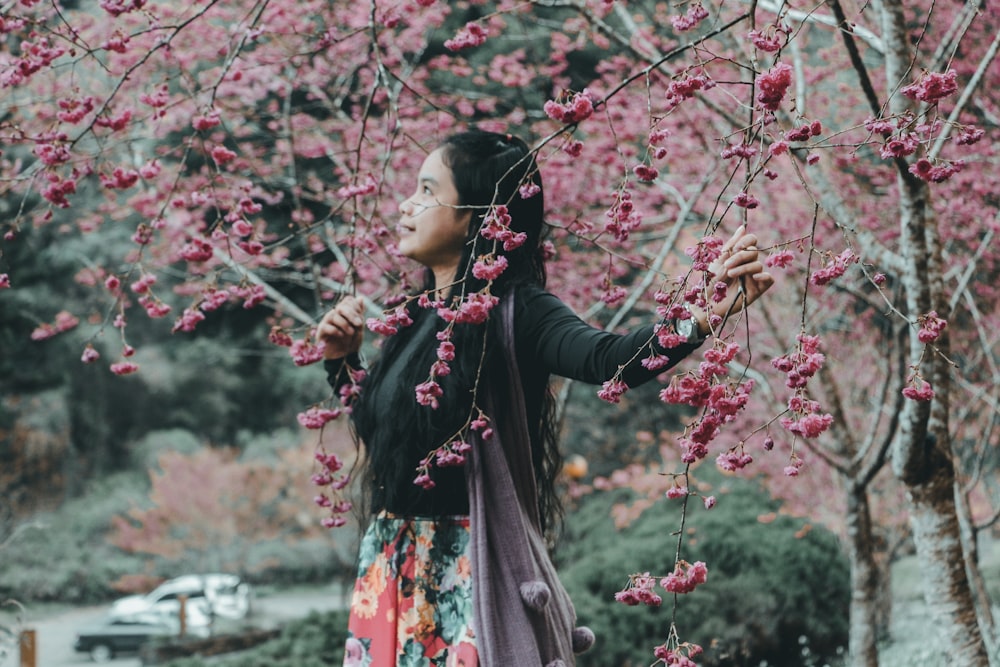 Mujer de pie bajo el árbol de flor de cerezo rosa durante el día