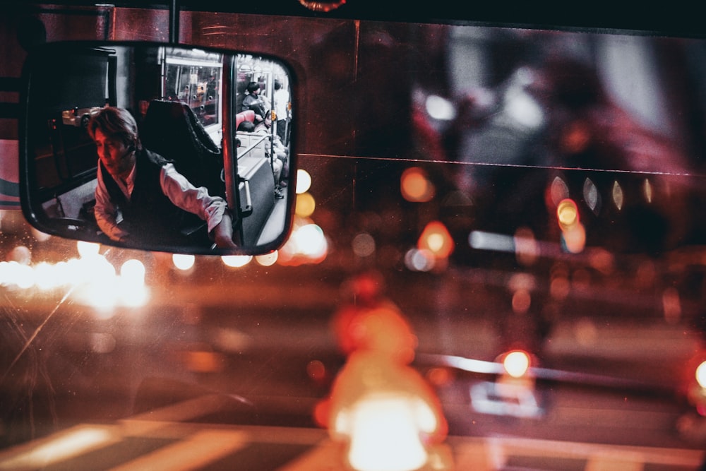 man wearing black vest with white dress shirt reflecting on rear-view mirror